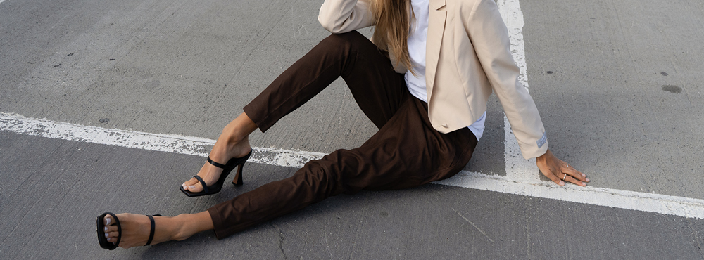 Kvinde der sidder på asfalt med brune læderbukser og stilletter