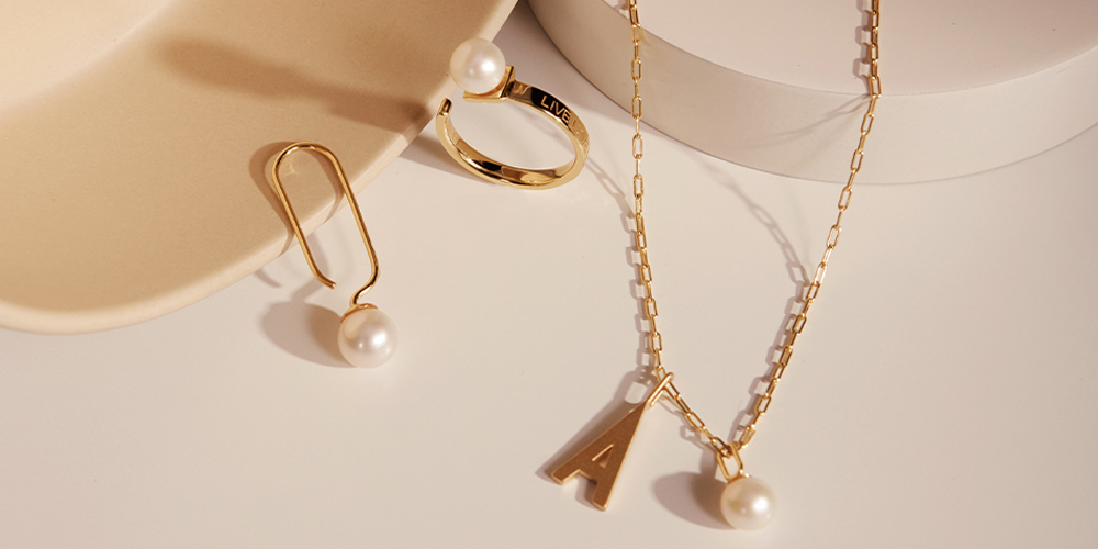 Guldsmykker med hvide perler; en ørering, en ring og en halskæde.