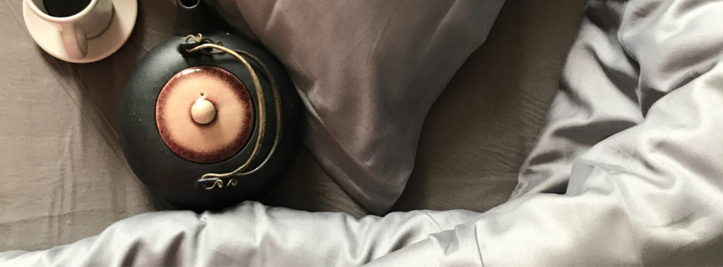 Et billede af sengetøj og en lille termokande i messing.