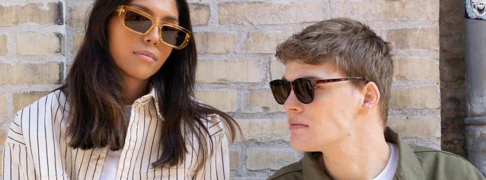 En kvinde og en mand sidder med solbriller på, købt fra Butler Loftet.